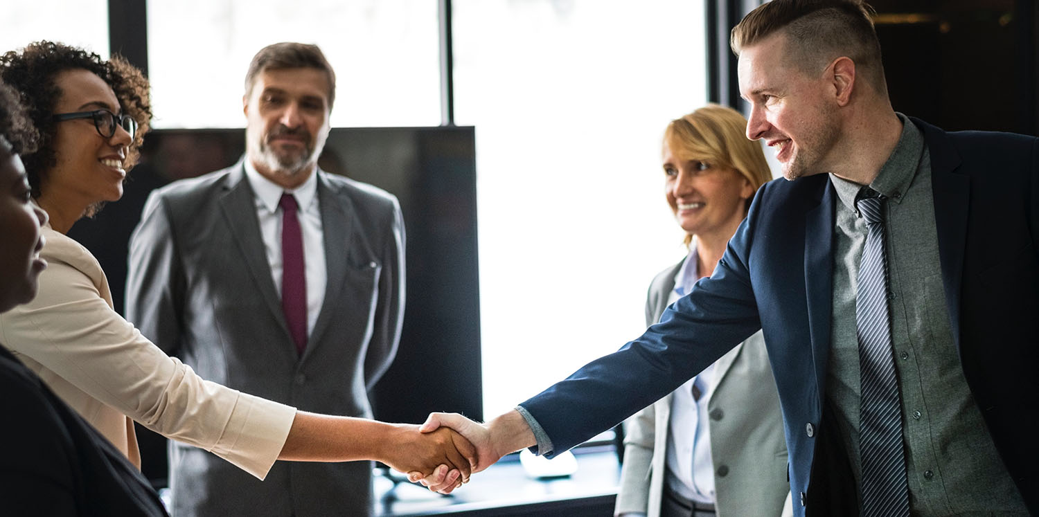 business man shaking hands with business woman while coworkers watch