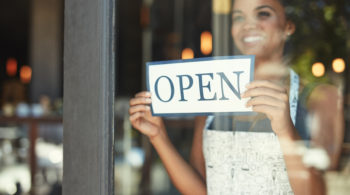 woman holding up open sign behind window