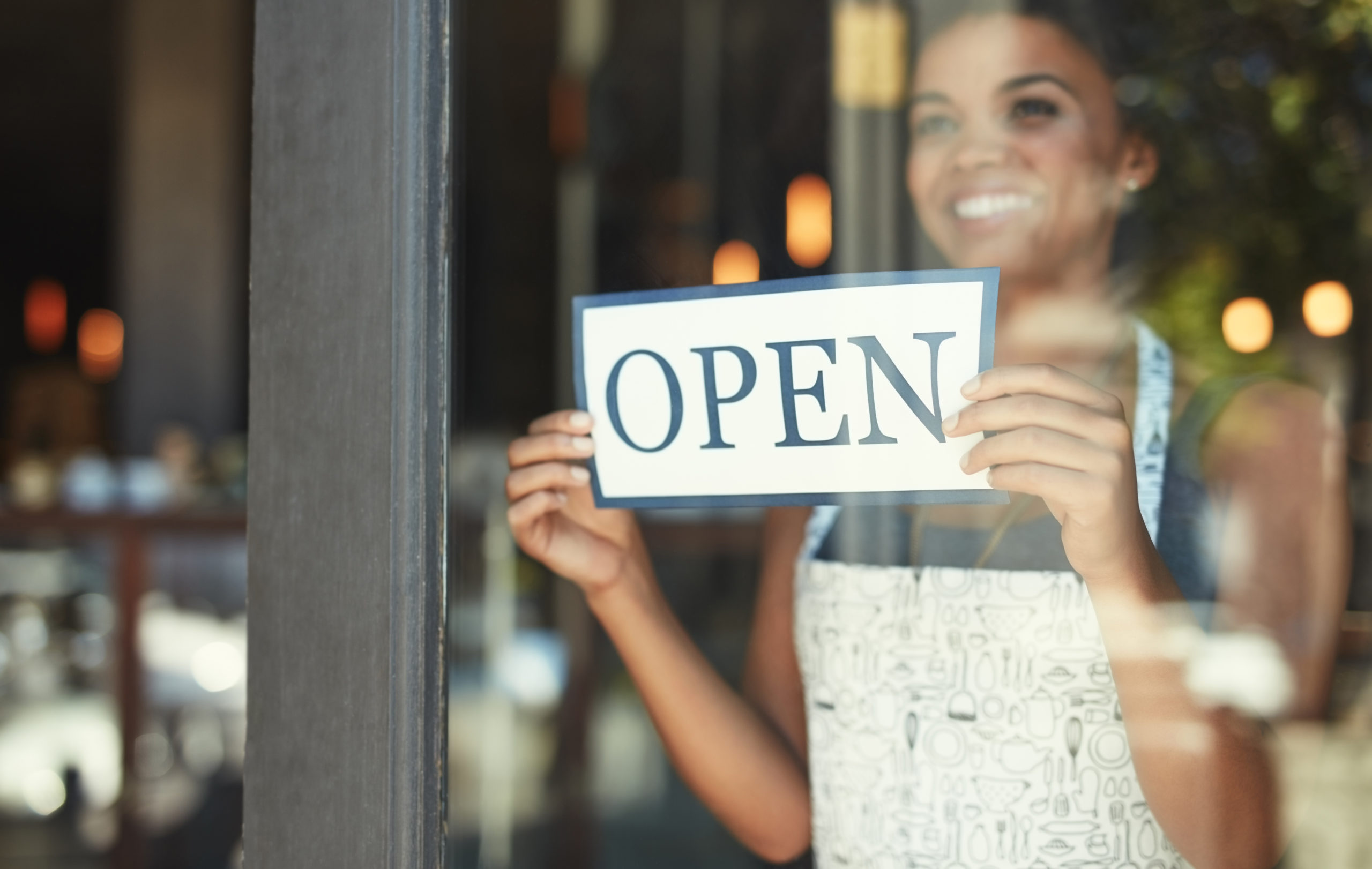 woman holding up open sign behind window