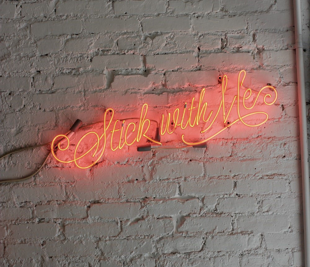 neon sign on wall that says stick with me