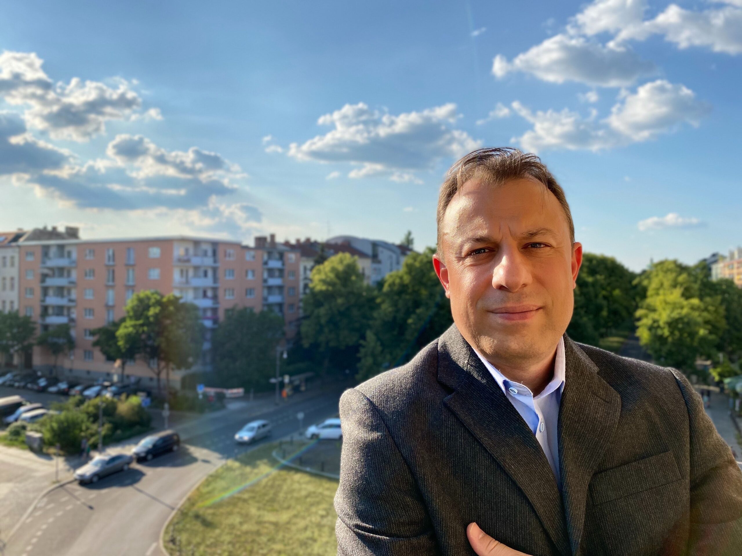 Man in suit with arms crossed standing on balcony in front of building