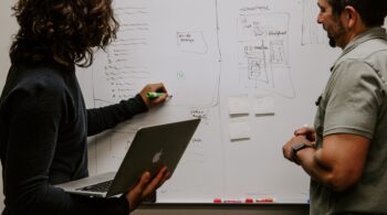 woman writing on whiteboard with dry erase marker while colleague watches