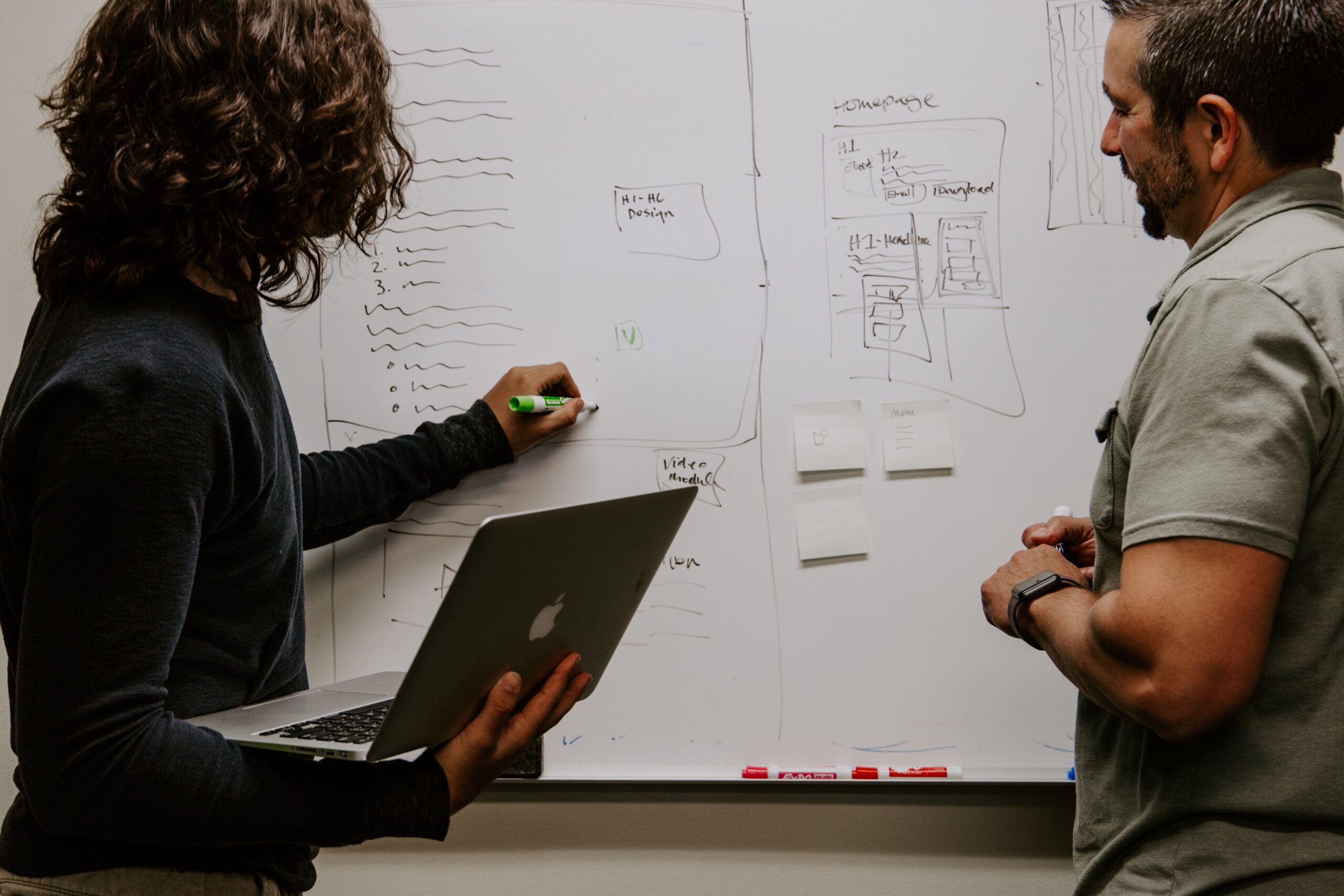 woman writing on whiteboard with dry erase marker while colleague watches
